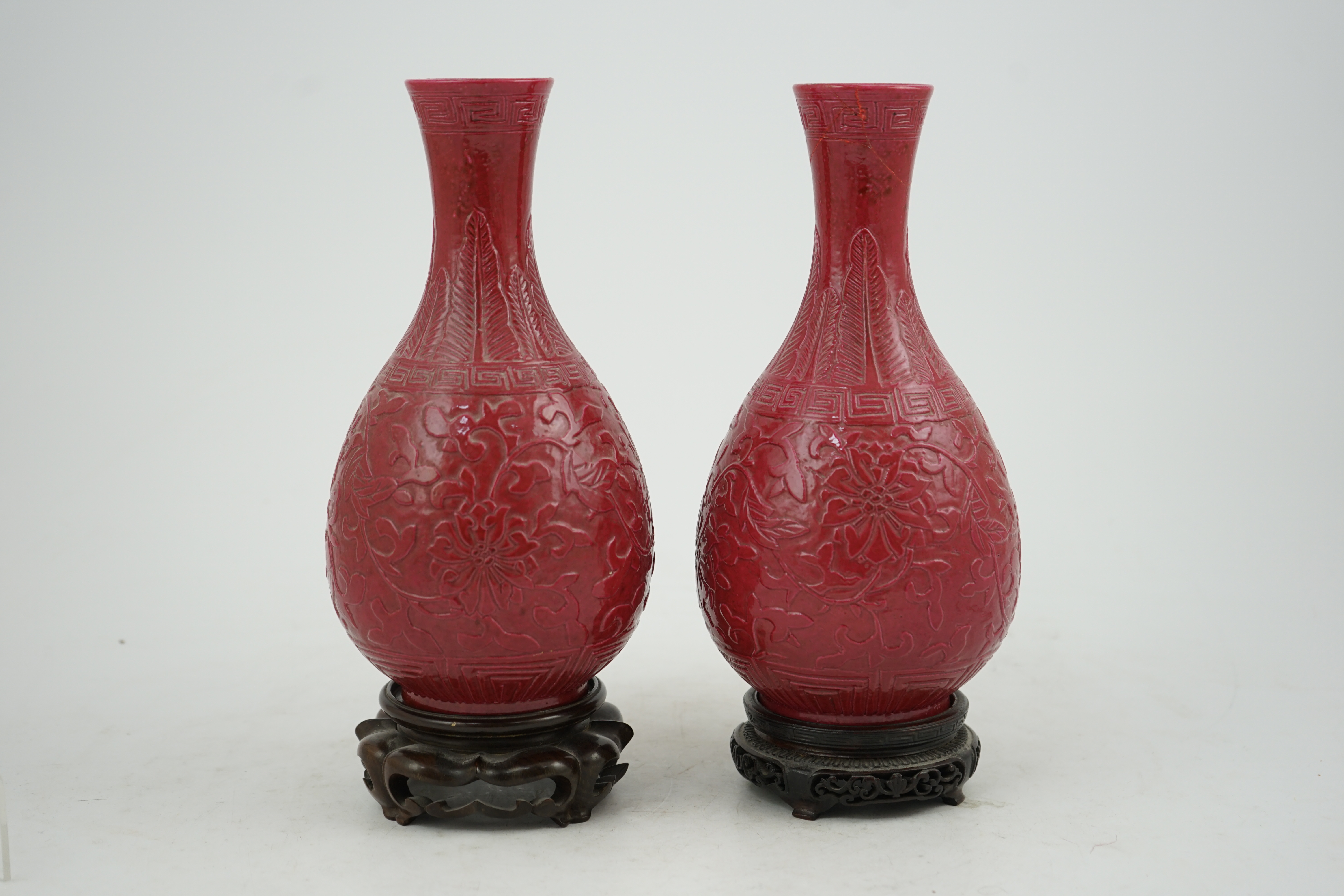 A pair of Chinese ruby ground ‘lotus’ bottle vases, late 19th century, each carved in relief with lotus flowers, scrolling tendrils and leaves, both with carved stands, 24cm high. Condition - one vase the neck broken bot